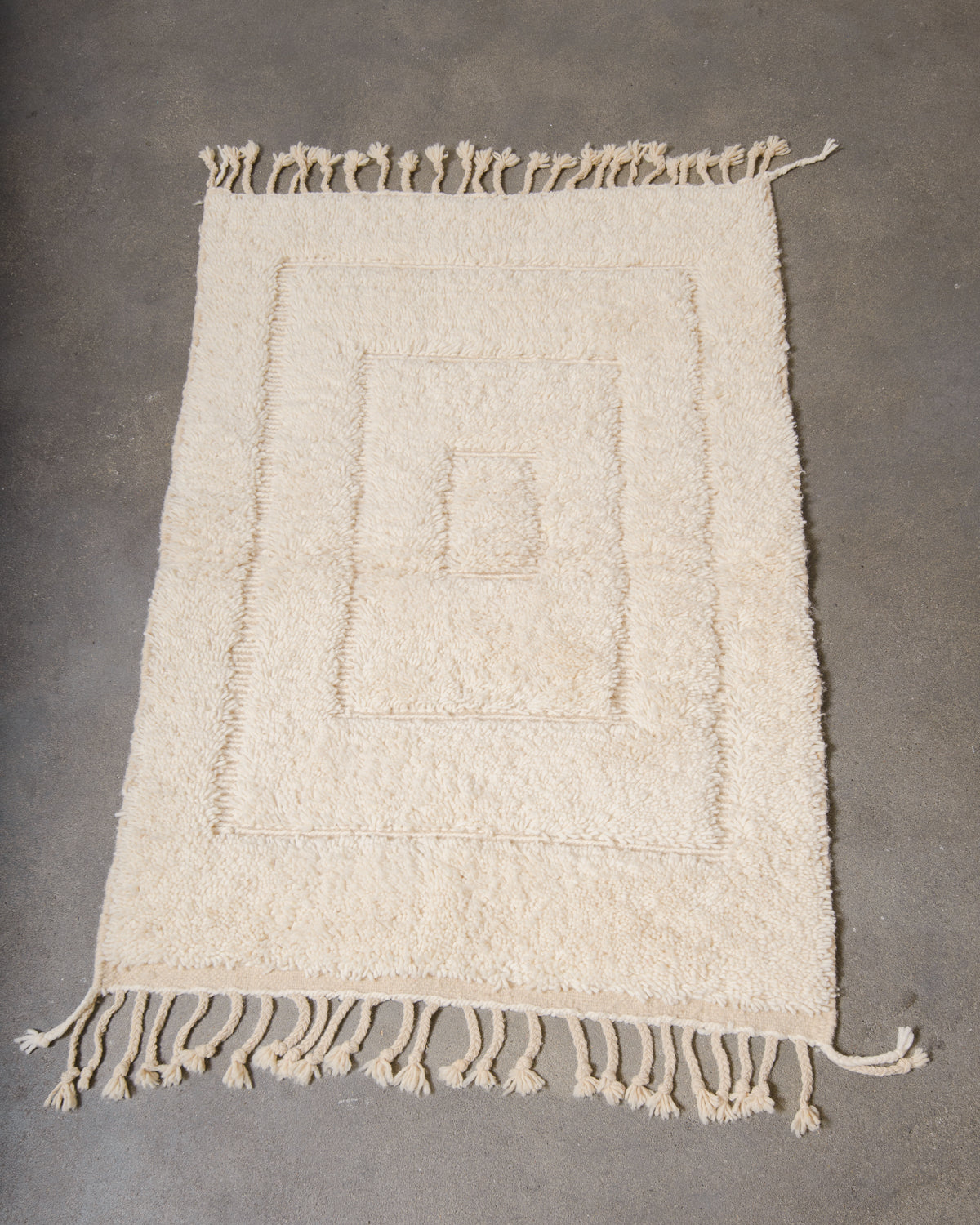 Beniourain rug in cream wool laying on concrete studio floor.